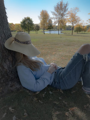A woman sleeping with a sun hat covering her face under a tree on a sunny day
